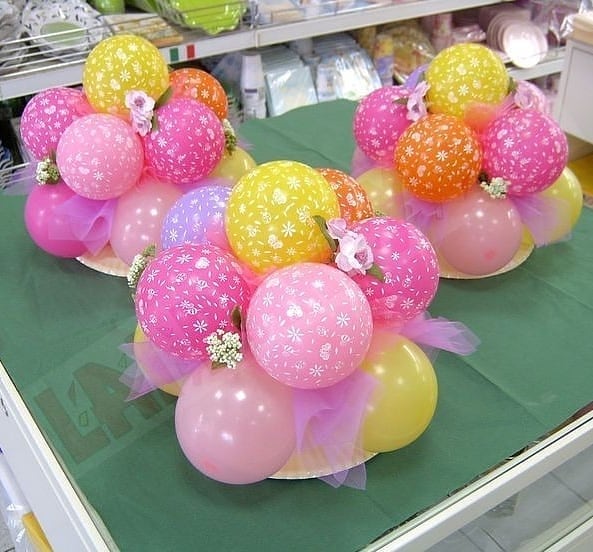 Centros de mesa com balões coloridos estampados, tule rosa e mini flores, dispostos sobre base redonda para decoração de festa infantil ou primavera.