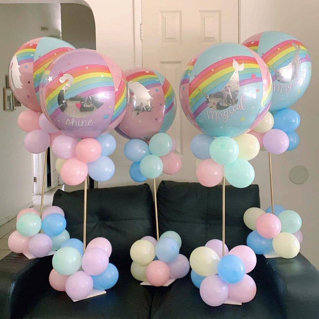 Centros de mesa com balões pastel e balões grandes com estampa de arco-íris e unicórnio, perfeitos para decoração de festa infantil mágica.