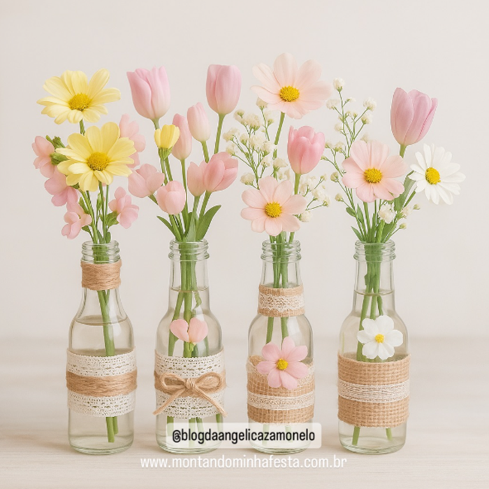 Garrafinhas decoradas com juta, renda e flores em tons pastel usadas como centro de mesa para festas.