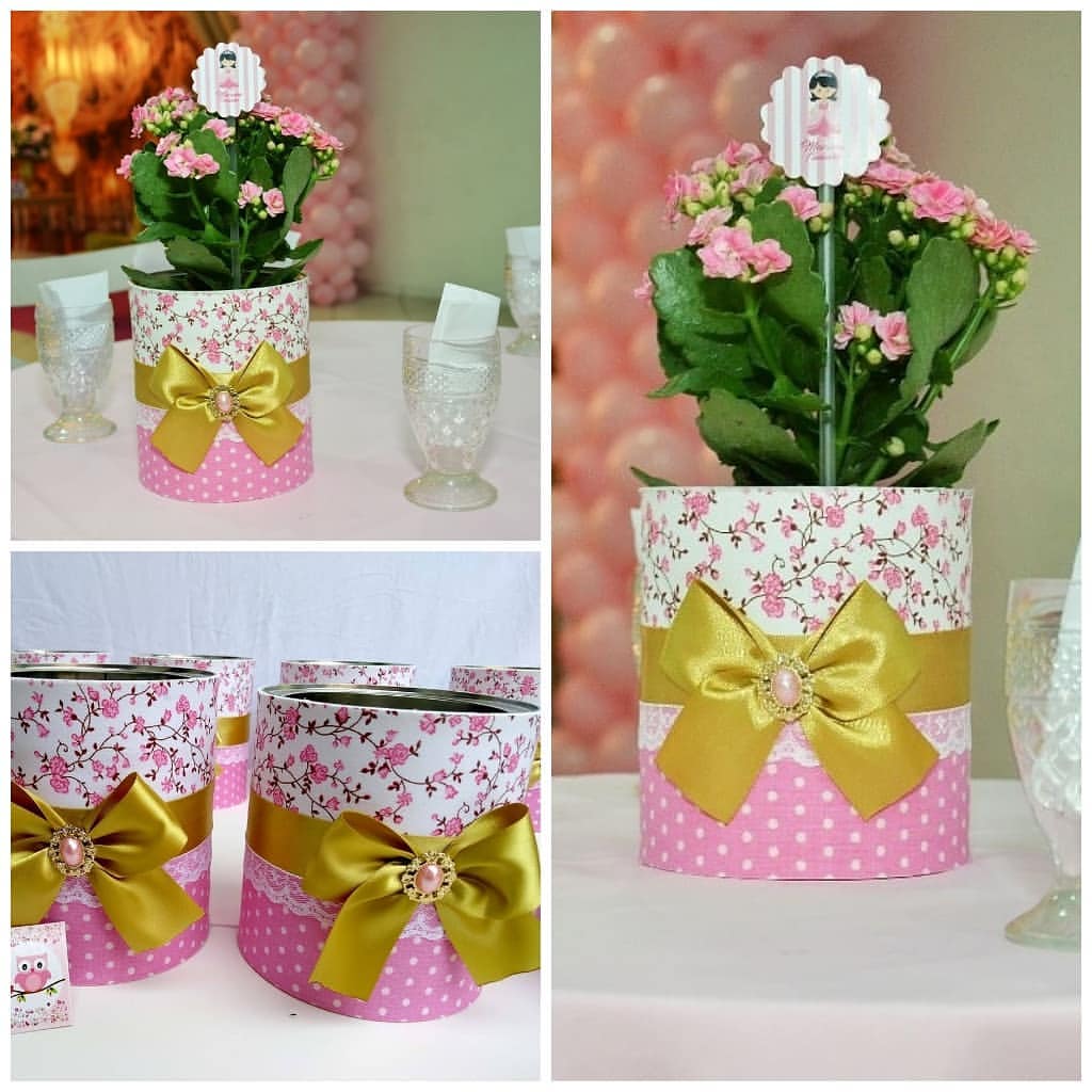 Centro de mesa com lata revestida em tecido floral e poá rosa, decorada com laço dourado e flor natural, estilo rústico e delicado para festas.