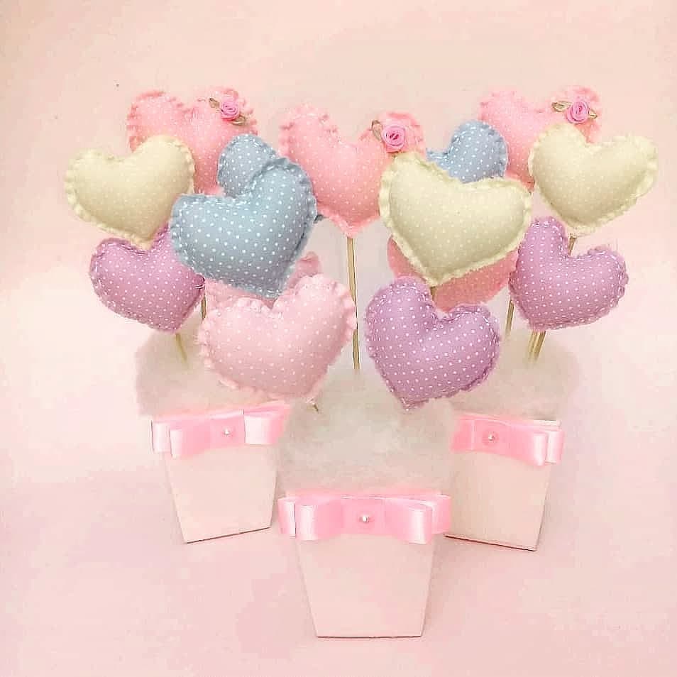 Centros de mesa com corações de tecido em tons pastel e poás, organizados em vasinhos brancos com laços de cetim rosa claro.