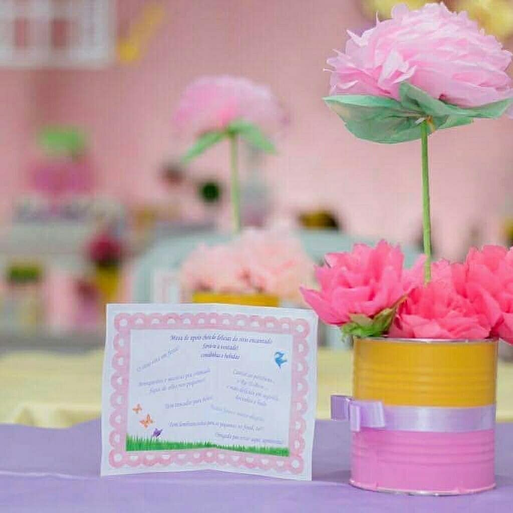 Centro de mesa com flor de papel seda rosa em lata reciclada pintada de amarelo e rosa com laço.