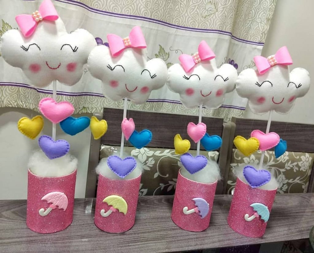 Centro de mesa feito com nuvem de feltro branco, corações coloridos e base rosa com glitter, perfeito para tema chuva de amor.