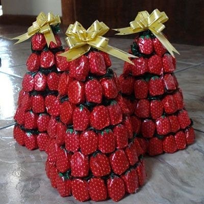 Centro de mesa pirâmide com balas de morango e laço dourado, ideal para decoração de festas.
