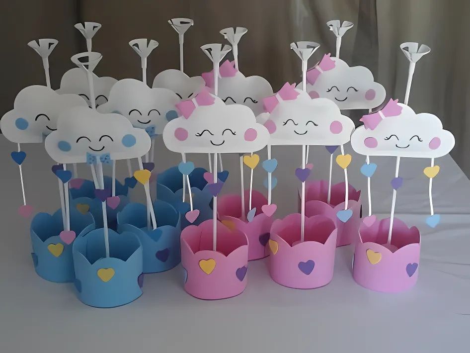 Centros de mesa em EVA com nuvens felizes, corações coloridos e base azul ou rosa, usados em festas infantis com tema Chuva de Amor para meninos e meninas.