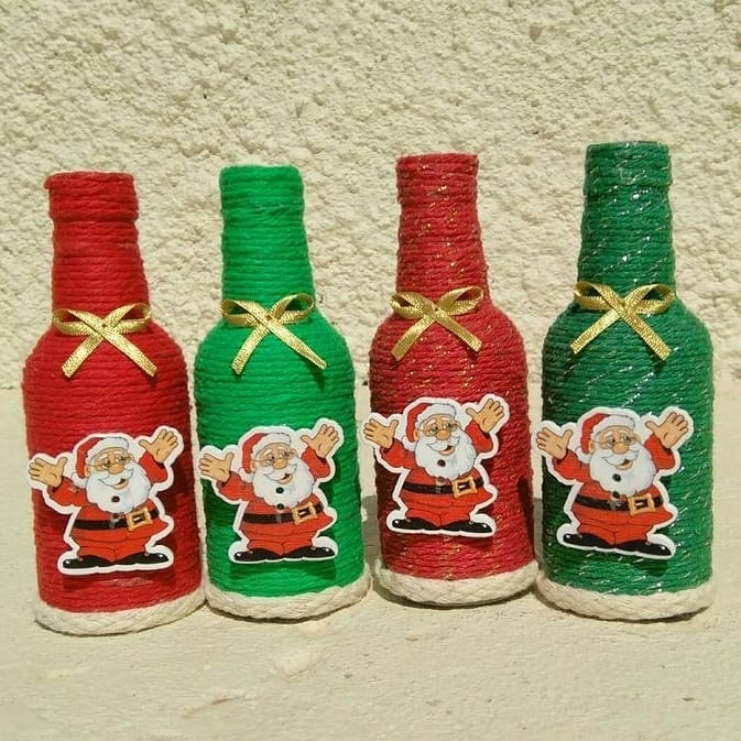 Garrafas decoradas com barbante vermelho e verde, adesivos de Papai Noel e laços dourados, usadas como centro de mesa ou enfeite de Natal artesanal.