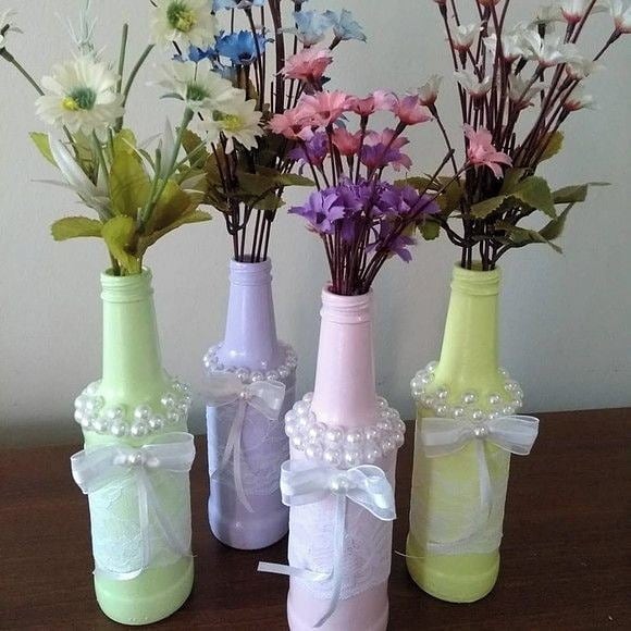Garrafas decoradas em tons pastel com renda, pérolas e laços de cetim, com flores artificiais, ideais como centro de mesa delicado para festas.