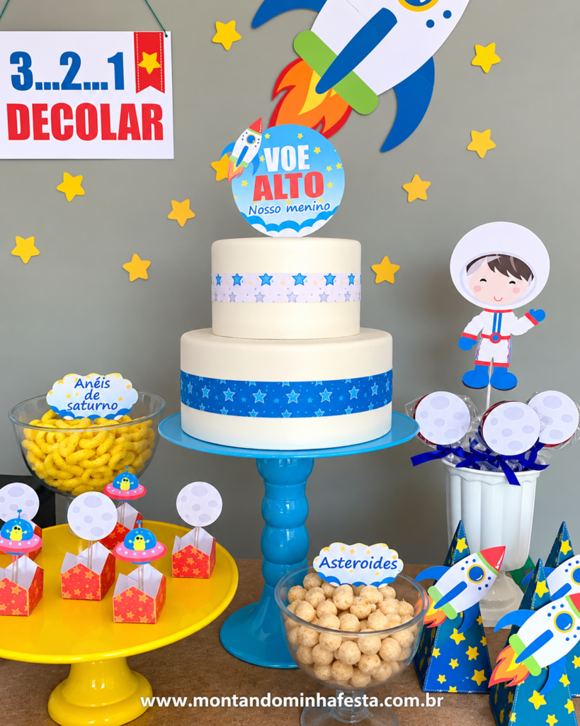 Bolo de dois andares para festa Astronauta, com topo de foguete, estrelas azuis, decoração espacial, lembrancinhas personalizadas e docinhos temáticos.