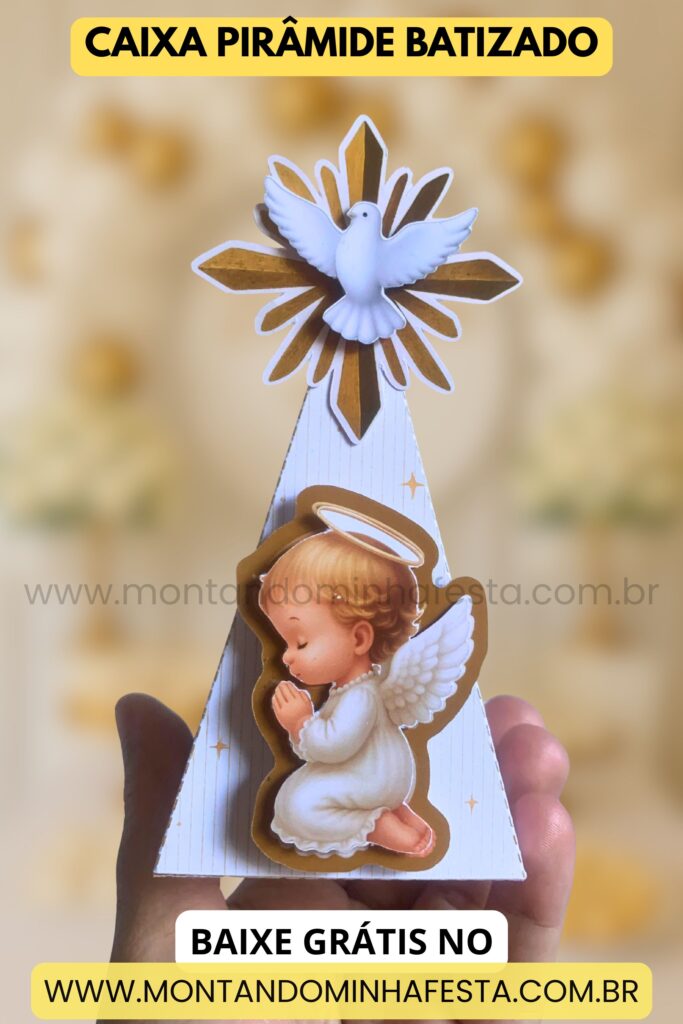 Foto real da caixa pirâmide para batizado com anjinho orando e Espírito Santo no topo, feita em papel impresso. Fundo desfocado com tons dourados e texto: “Baixe grátis no www.montandominhafesta.com.br”.